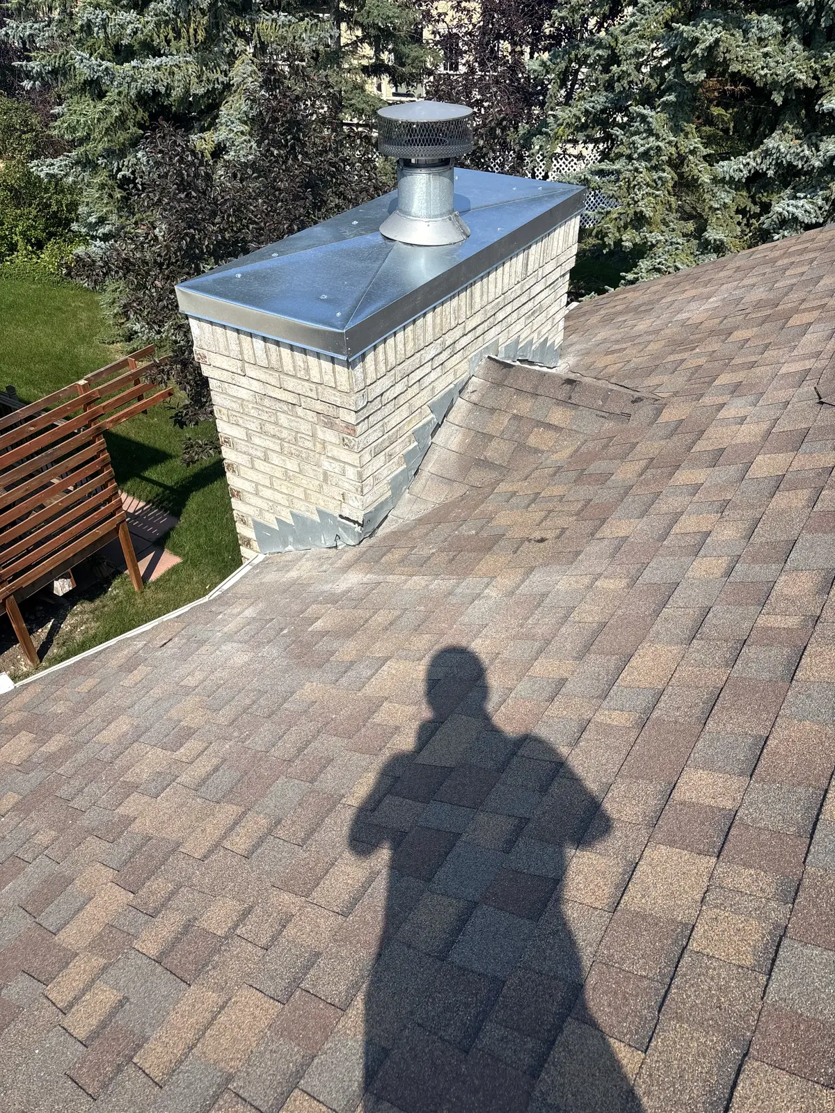 Repaired block chimney on a Calgary roof with a new metal cap and flashing tied into the shingles