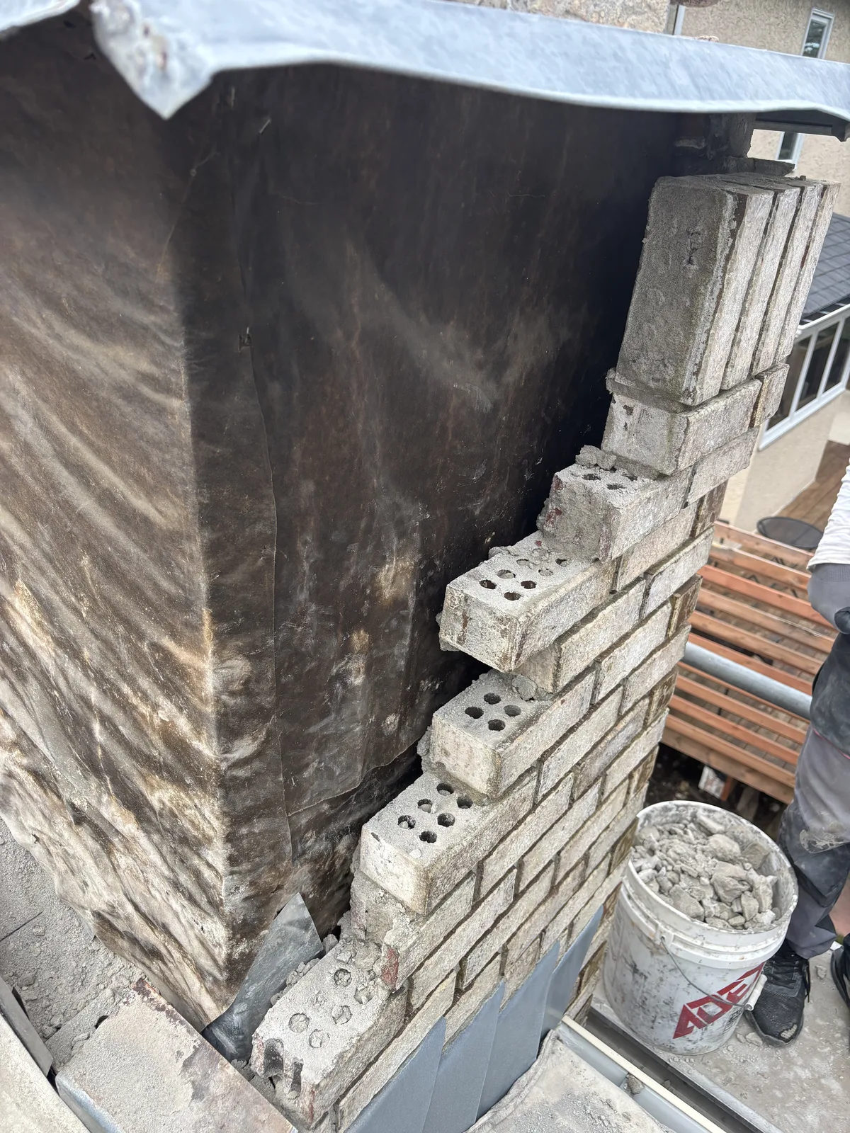 Brick chimney being rebuilt on a Calgary roof, new courses going up over the wrapped base