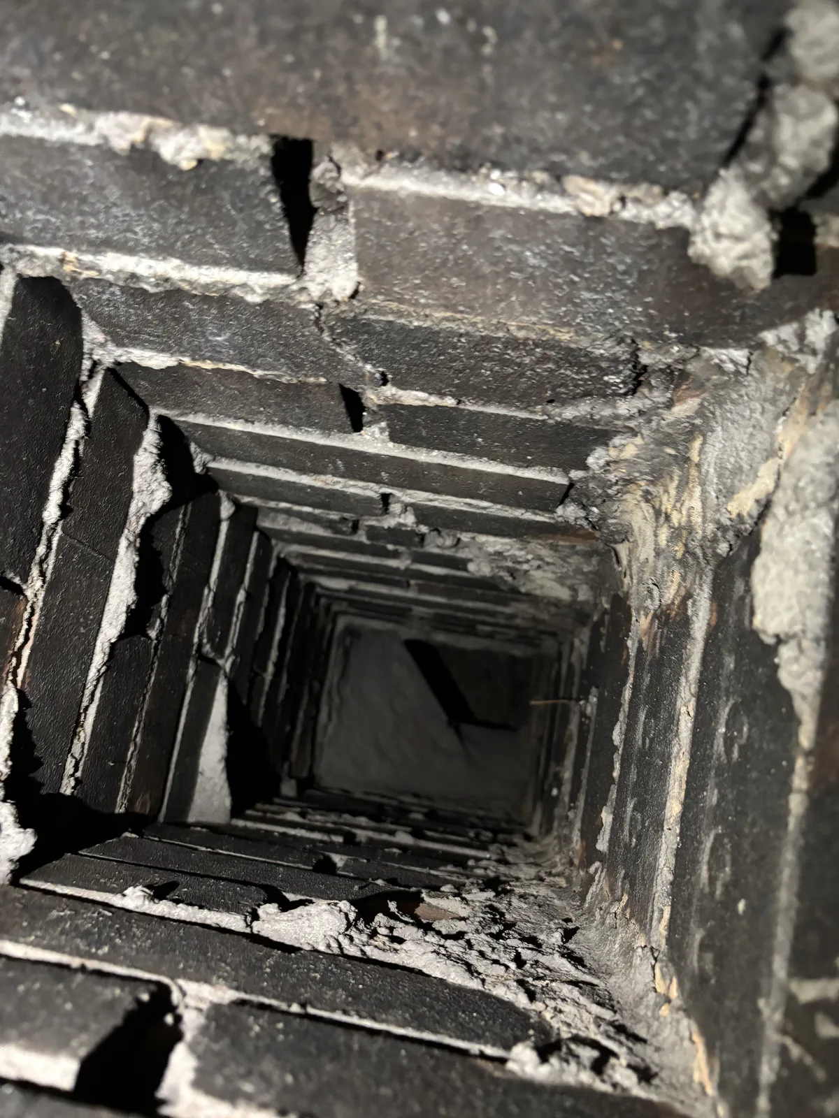 Looking down the flue of a Calgary brick chimney during repair, loose mortar and soot on the inside faces