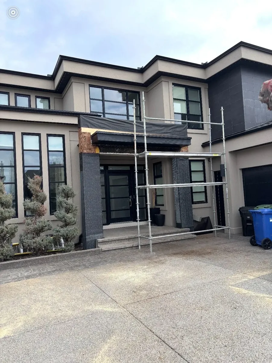 Calgary luxury home exterior entryway during tile installation — scaffolding up, dark underlayment and membrane exposed where porcelain cladding will go