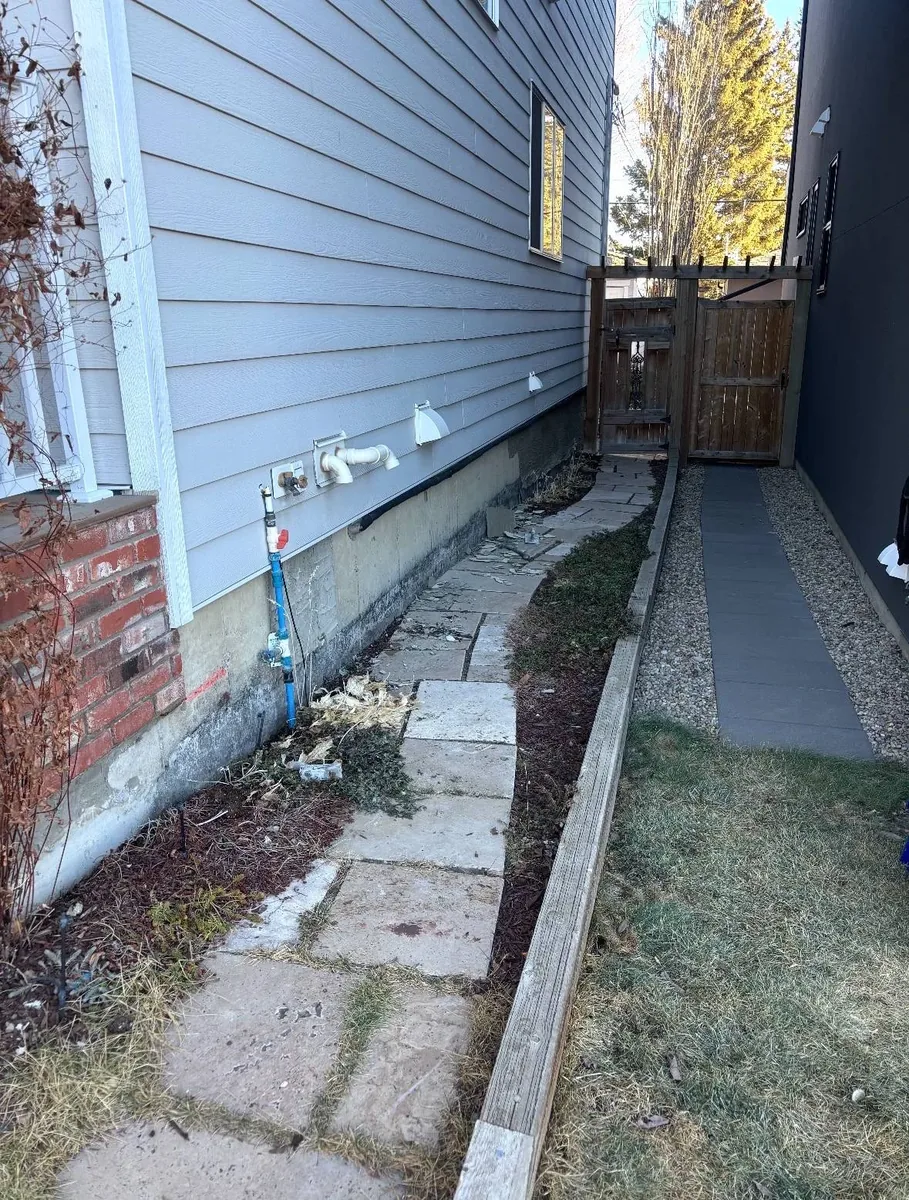 Calgary sidewall foundation before parging — bare weathered concrete with no parging coat, gas line and meter visible at base