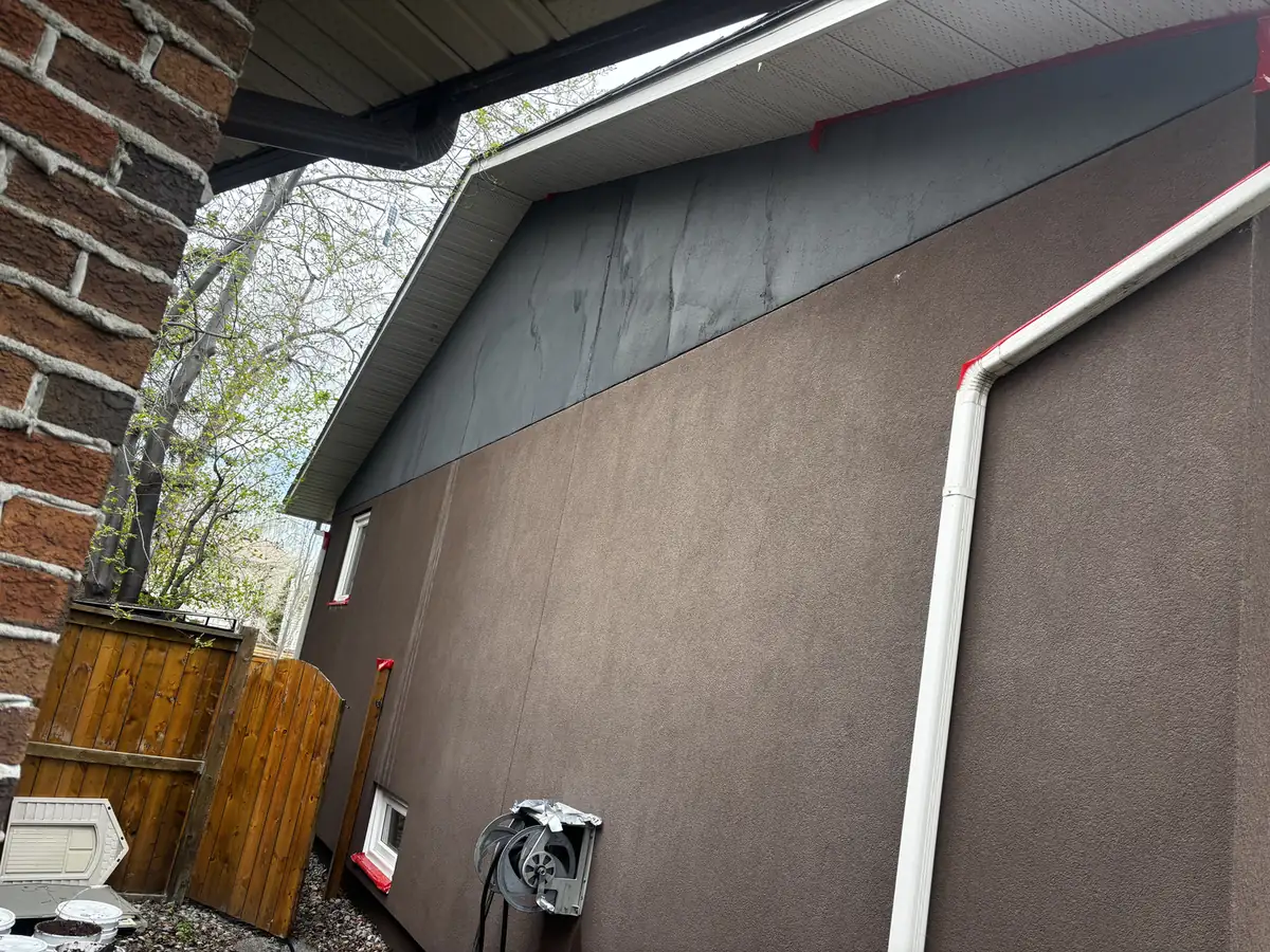 Graphex coat being applied to a Calgary gable wall, edges masked in red tape