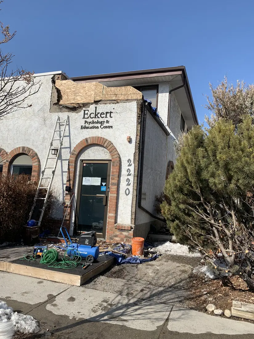 Calgary commercial storefront mid-restoration, stucco cut back over brick arch and sheathing exposed