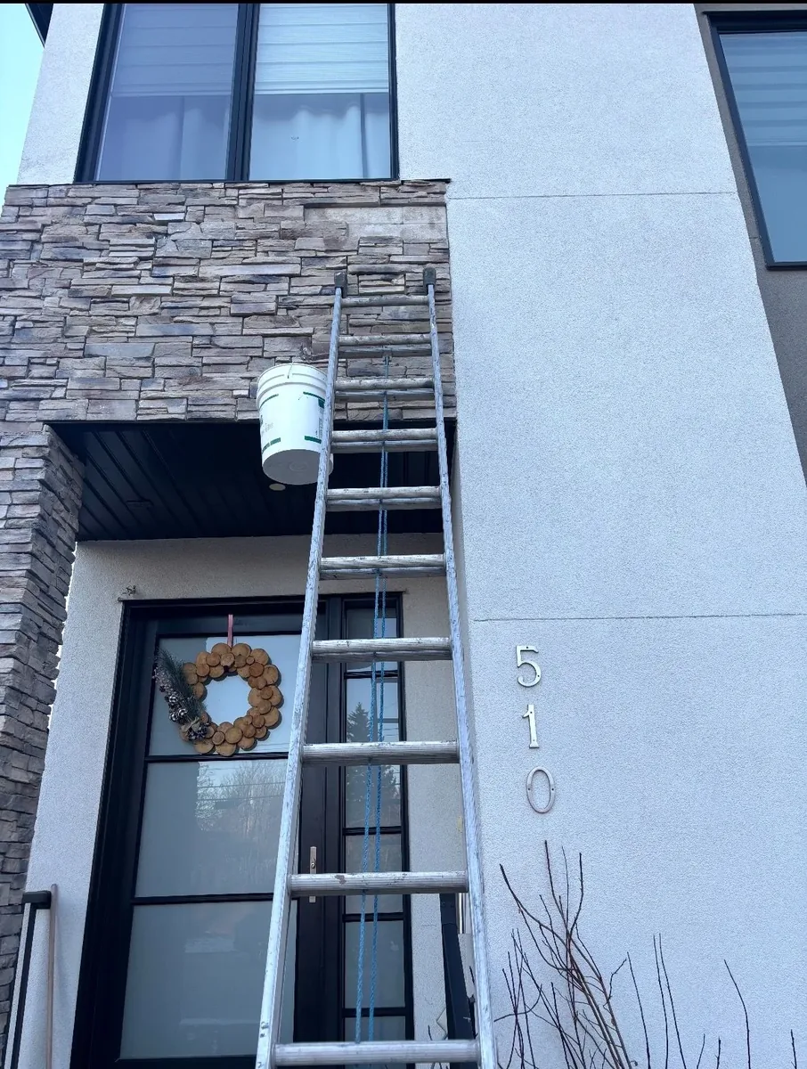 Calgary stone facade falling repair before — fallen stones at the top edge of the veneer, ladder and bucket in place mid-repair
