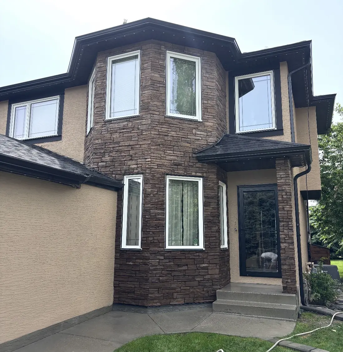 Calgary two-storey entry turret after cladding — floor-to-roofline stacked stone veneer around the windows and entry