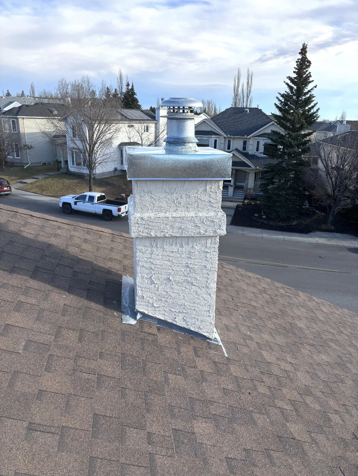 Stucco chimney on a Calgary roof with its new metal cap on, about to be patched and painted