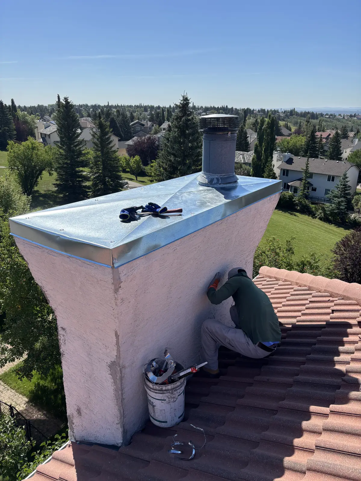 Stucco chimney chase on a tile roof in Calgary, new metal cap on and the stucco being patched and painted