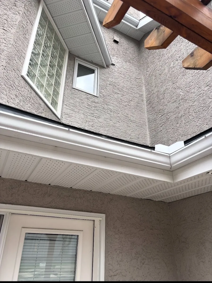 Calgary stucco eave corner before repair — aged patchy stucco with moisture damage near soffit