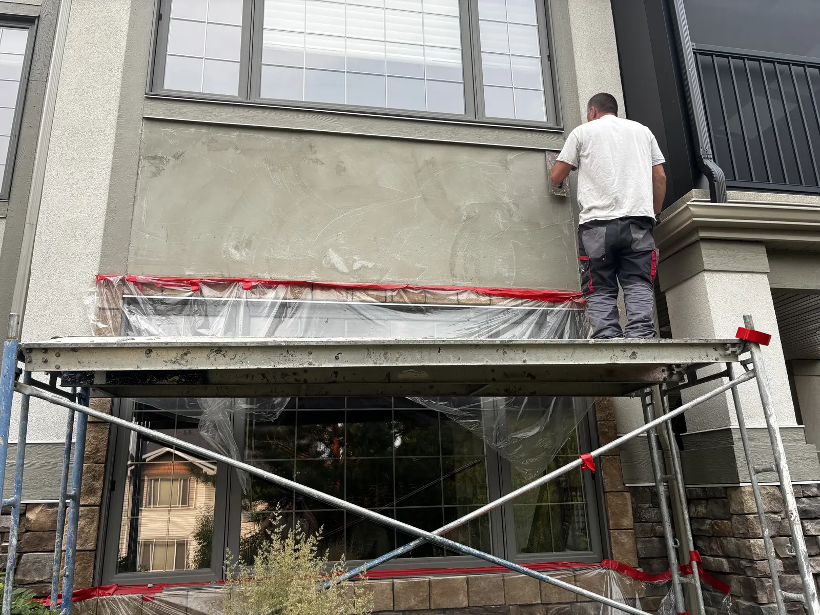 Calgary Stucco and Slate crew member on scaffold applying base coat over a stucco crack repair on a two-storey Calgary home