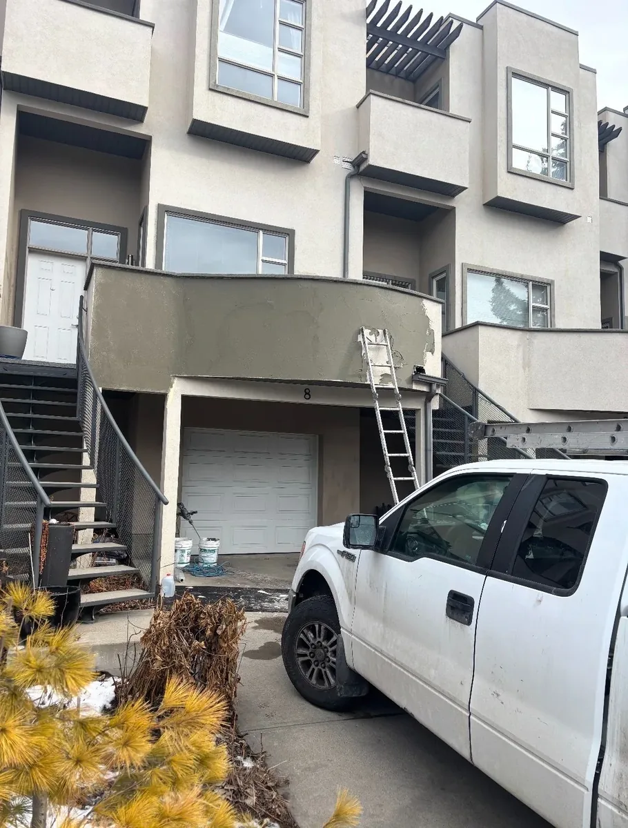 Calgary townhouse stucco re-coat in progress — failing balcony band with patchy finish before re-coat