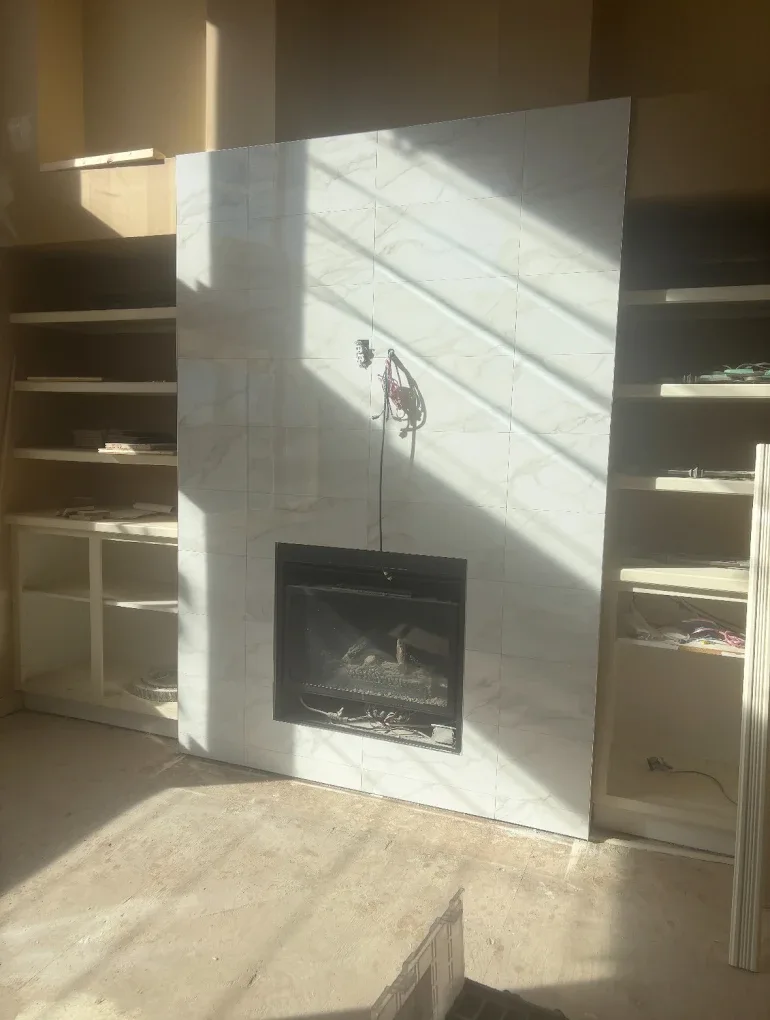 Calgary tile fireplace after install — clean large-format marble-look porcelain cladding around the fireplace insert with built-in shelving flanking each side