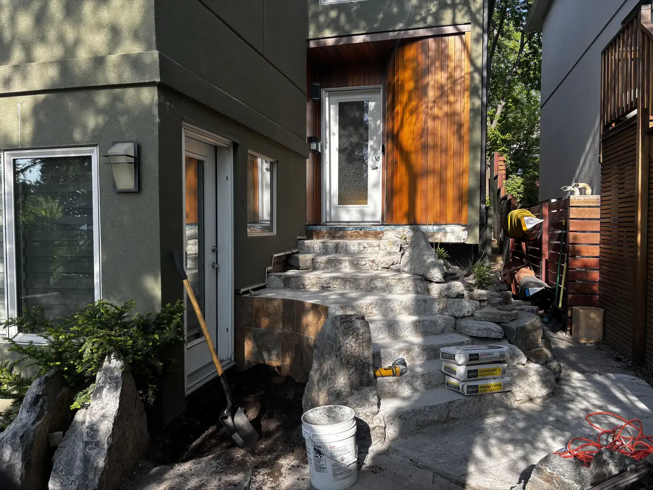 Calgary front entry stairs mid-rebuild, rough stone steps with tools and concrete bags on site